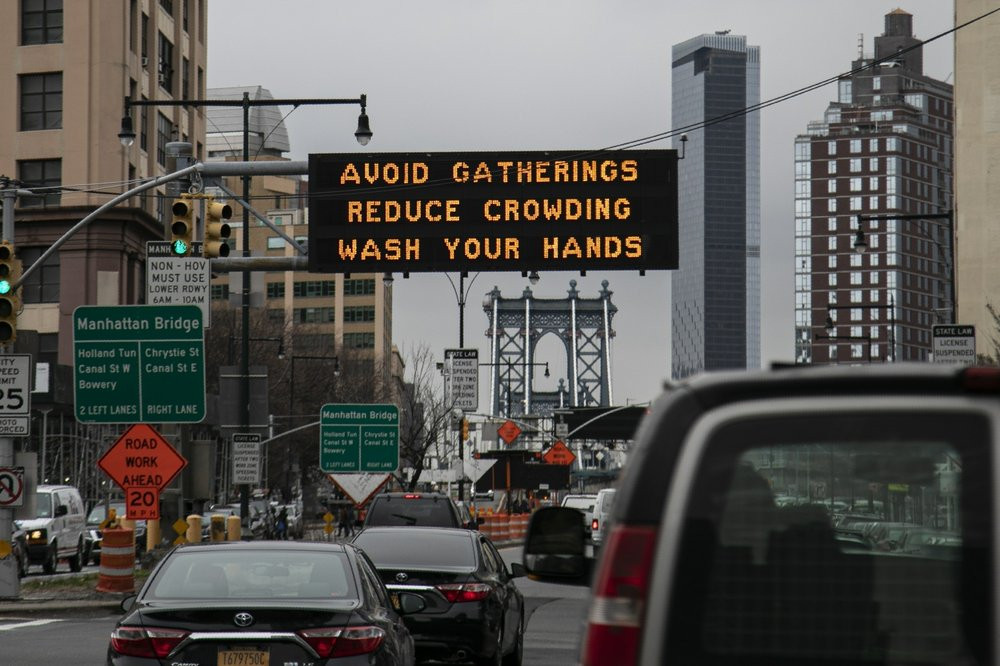 In this March 19, 2020, file photo, the Manhattan bridge is seen in the background of a flashing sign urging commuters to avoid gatherings, reduce crowding and to wash hands in the Brooklyn b