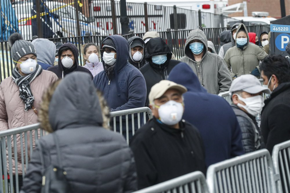 Patients wear personal protective equipment while maintaining social distancing as they wait in line for a COVID-19 test at Elmhurst Hospital Center, Wednesday, March 25, 2020, in New York.
