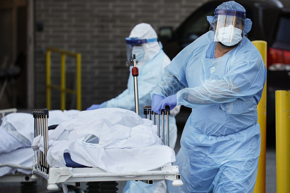 Medical workers wearing personal protective equipment wheel bodies to a refrigerated trailer serving as a makeshift morgue at Wyckoff Heights Medical Center, Monday, April 6, 2020, in the Bro