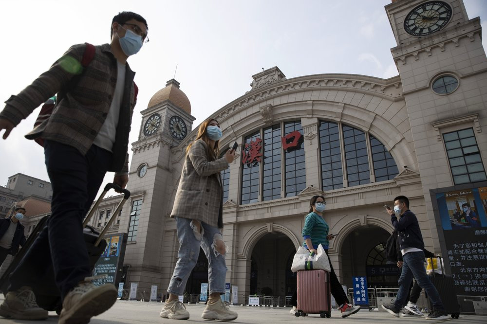 Travelers with their luggage walk past the Hankou railway station on the eve of its resuming outbound traffic in Wuhan in central China's Hubei province on Tuesday, April 7, 2020.