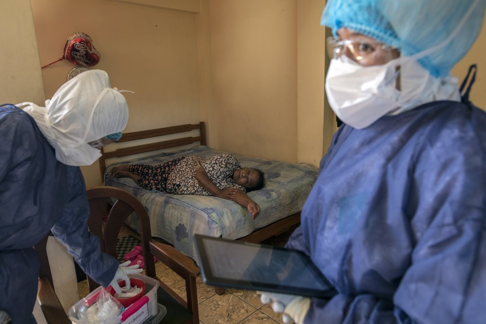 Maria Teresa Carrillo, 87, rests in a bed as Doctor Leslei Montoro, left, and her colleague Doctor Carolina Quiroz, check a sample for a new coronavirus fast test, in Lima, Peru, Wednesday, A
