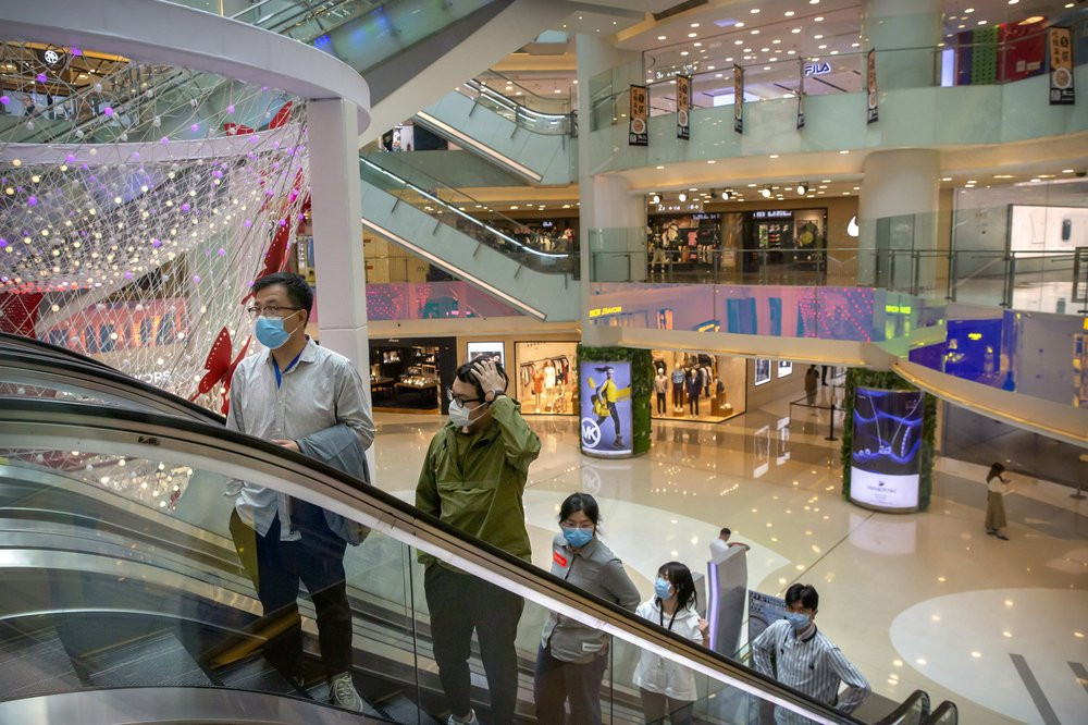 In this April 15, 2020 photo, people wear facemasks to protect against the spread of the new coronavirus cleans as they ride an escalator at a shopping mall in Beijing.
