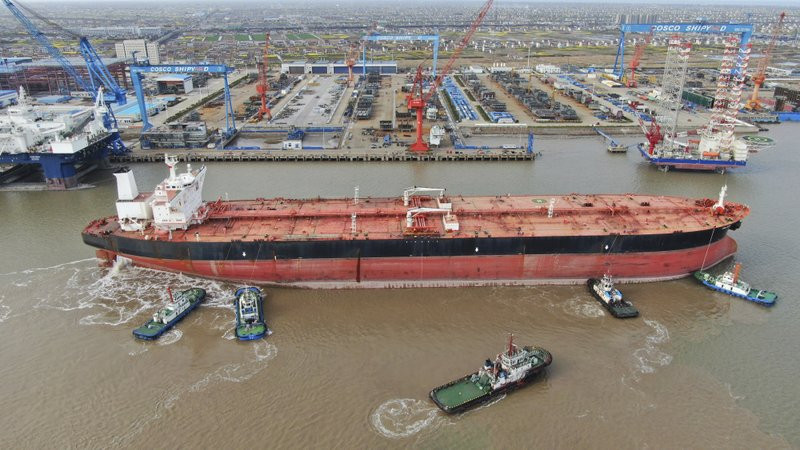 In this photo taken Monday, March 16, 2020, tugboats push a 300,000-ton very large crude carrier (VLCC) to a shipyard on the Yangtze River for retrofit in Qidong city in east China's Jiangsu 