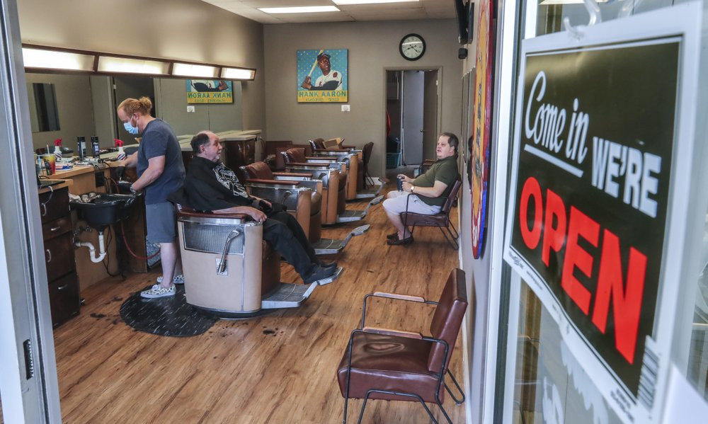Barber and owner of Chris Edwards, left, wears a mask and cuts the hair of customer at Peachtree Battle Barber Shop in Atlanta on Friday, April 24, 2020.