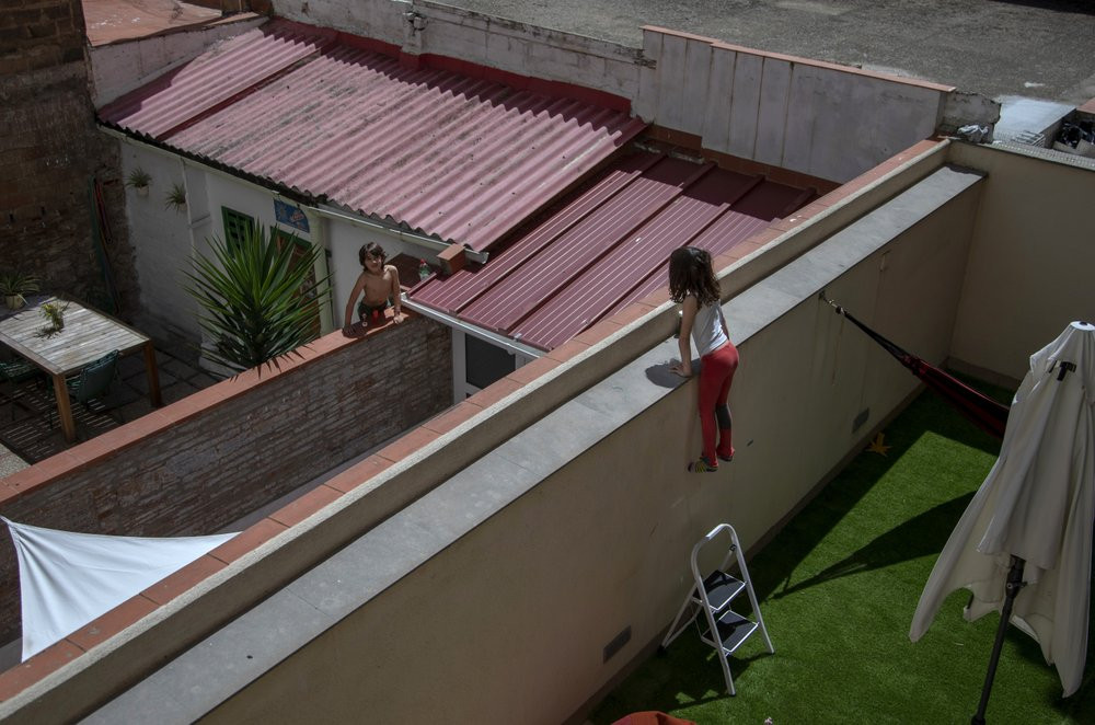 Gala, 7, speaks with her friend and classmate Oliver, 6, as they jump on the wall on their courtyard in Barcelona, Spain, Wednesday, April 29, 2020 as the lockdown to combat the spread of cor