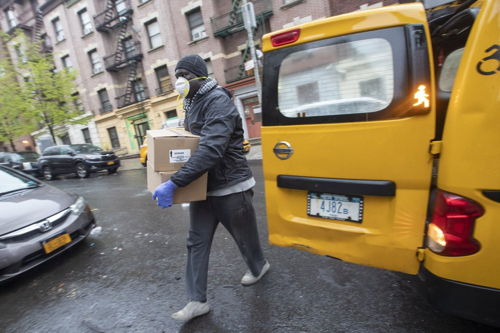Taxi driver Mor Gob, wearing a mask to protect against coronavirus, delivers boxes with prepared meals to people in need in the Bronx borough of New York, Thursday, April 30, 2020.