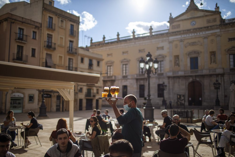 A waiter carries beers for customers sitting on a terrace bar in Tarragona, Spain, Monday, May 11, 2020.