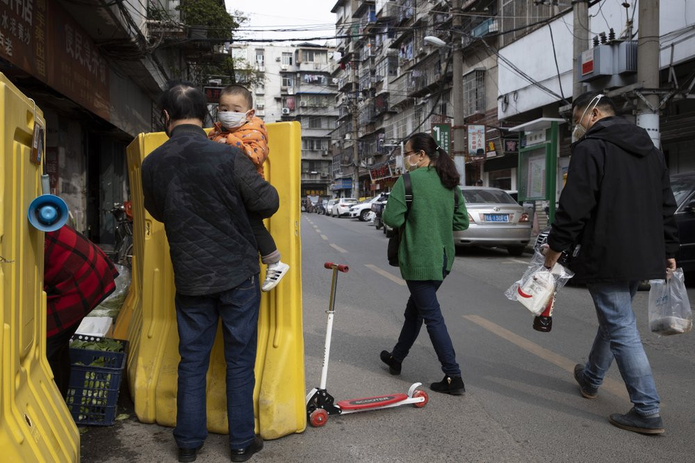 In this photo taken Wednesday, April 1, 2020, residents walk past a sealed off neighborhood in Wuhan, central China's Hubei province.