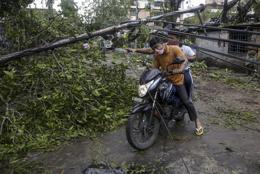 People make their way through damaged cables and a tree branch fallen in the middle of a road after Cyclone Amphan hit the region in Kolkata, India, Thursday, May 21, 2020.