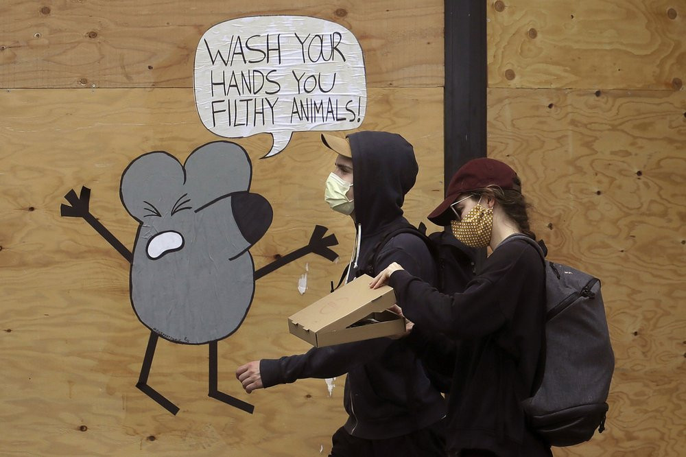 - In this May 2, 2020, file photo, a man and woman wearing masks to prevent the spread of the coronavirus walk past a cartoon advising people to wash their hands on a boarded up storefront in