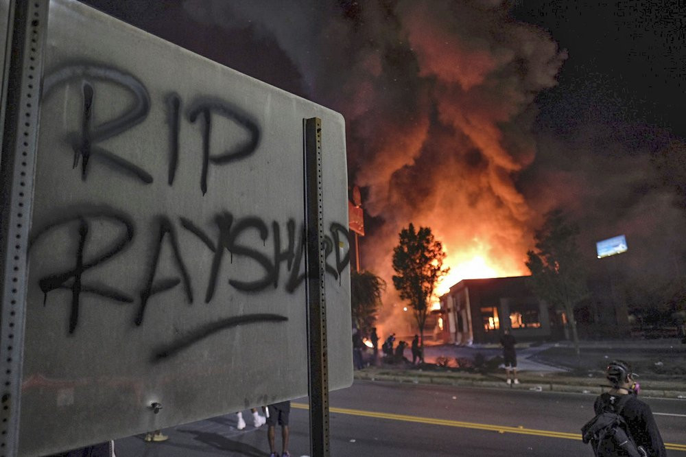 A Wendy's restaurant, background, burns Saturday, June 13, 2020, in Atlanta after demonstrators allegedly set it on fire. Demonstrators were protesting the death of Rayshard Brooks, a black m