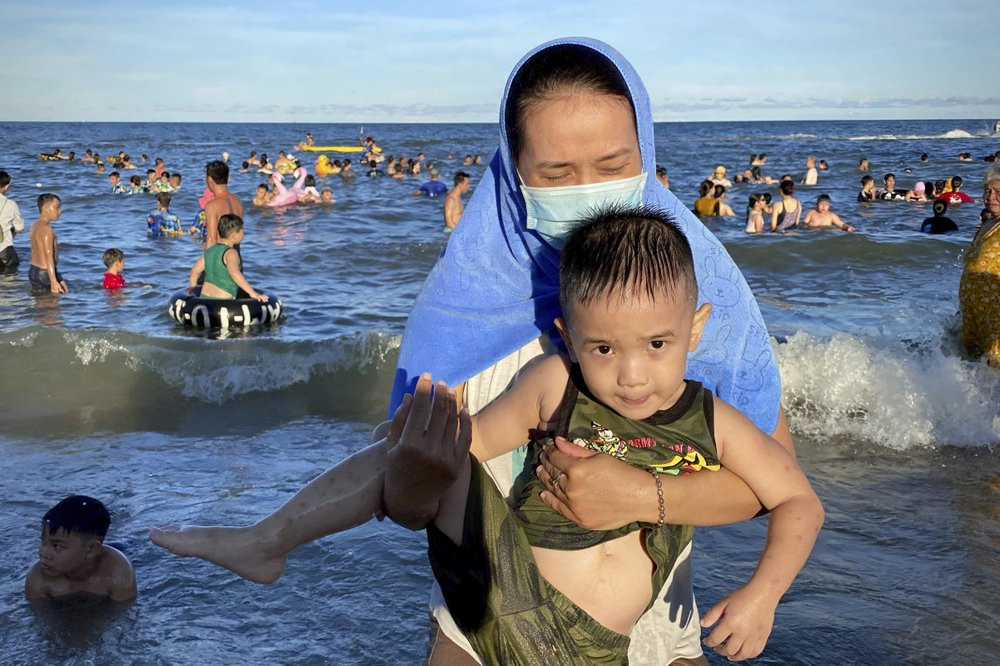 A woman wearing a mask carries her child on a beach in Vung Tau city, Vietnam, Sunday, July 26, 2020.