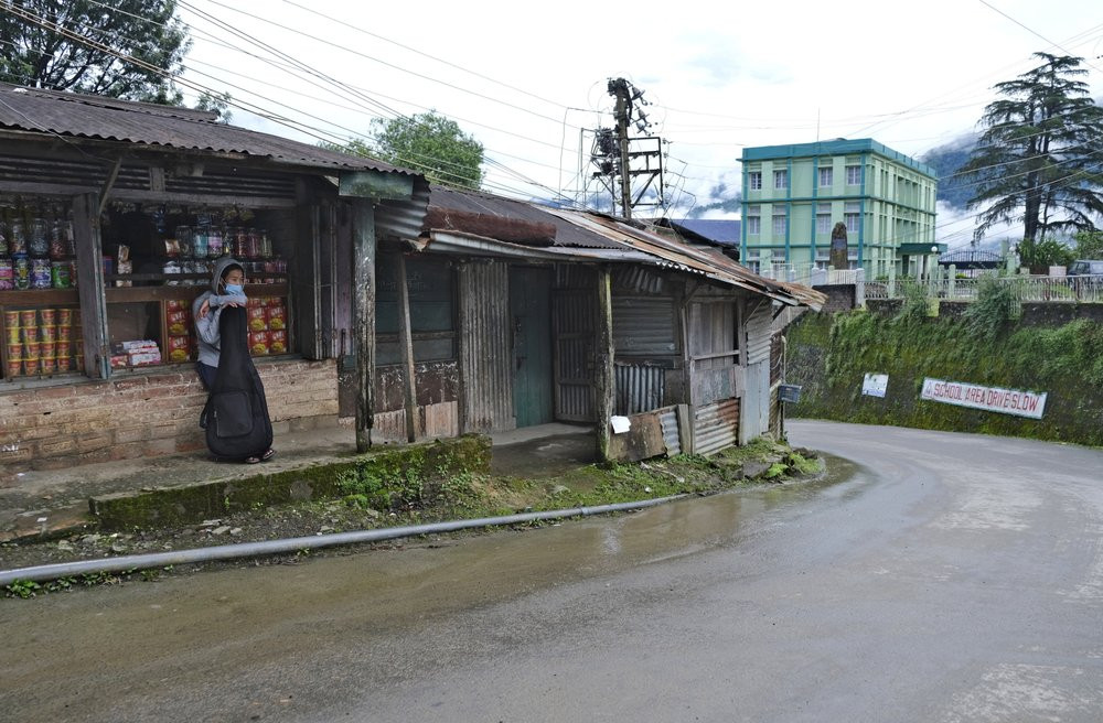 A Naga wearing a face mask leans on a guitar and sits by a deserted road in Kohima, capital of the northeastern Indian state of Nagaland, Thursday, Aug. 13, 2020.