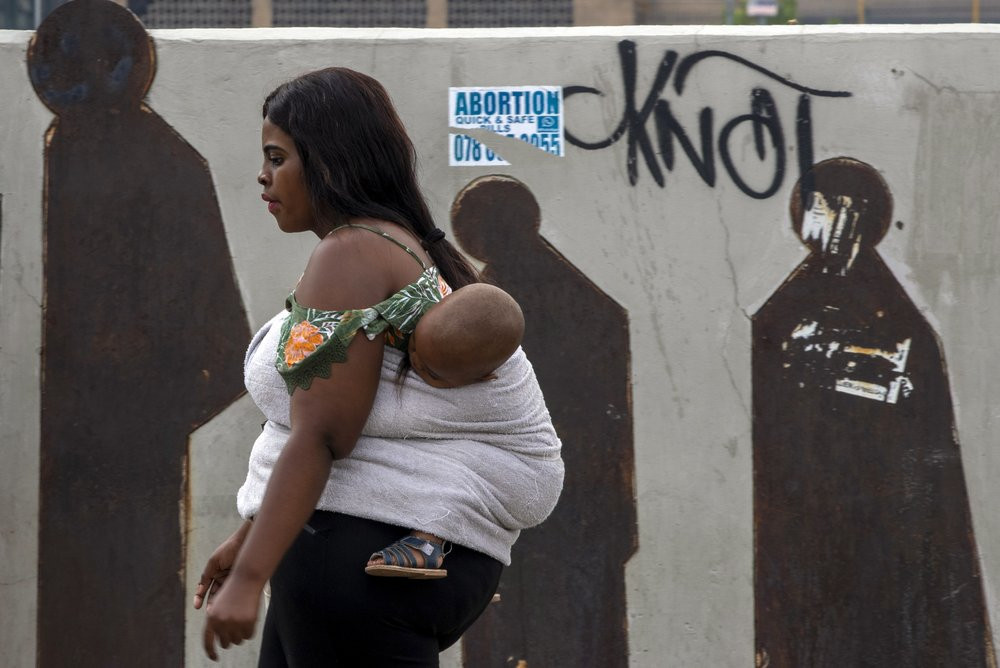 A  woman carrying her baby walks along a downtown street in Johannesburg, South Africa, Monday, March 16, 2020.