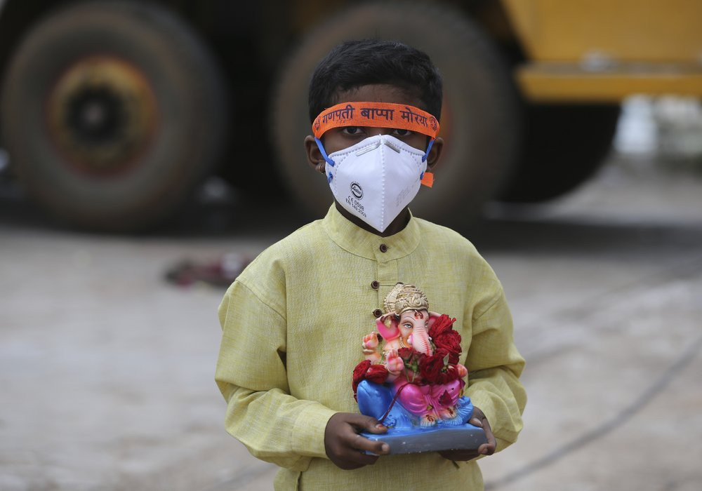 An Indian child wearing a mask as a precaution against the coronavirus carries an idol of elephant-headed Hindu god Ganesha to immerse in Saroornagar Lake on the final day of Ganesh Chaturthi