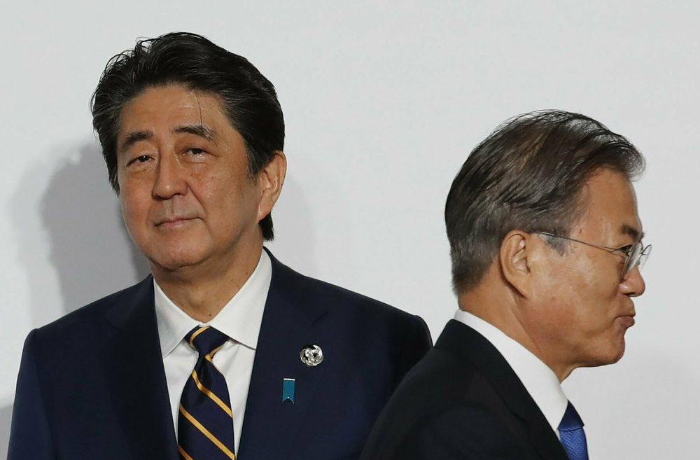 In this June 28, 2019, file photo, South Korean President Moon Jae-in, right, walks by Japanese Prime Minister Shinzo Abe upon his arrival for a welcome and family photo session at the G-20 l