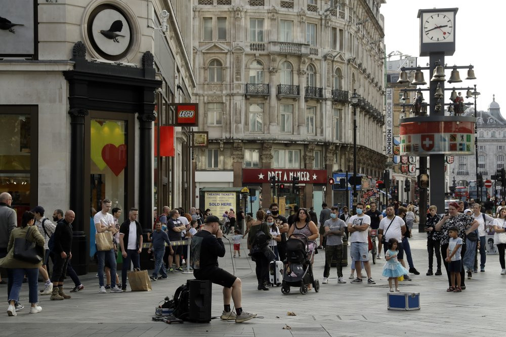 People listen to an entertainer perform in Leicester Square, central London, Saturday, Sept. 19, 2020.