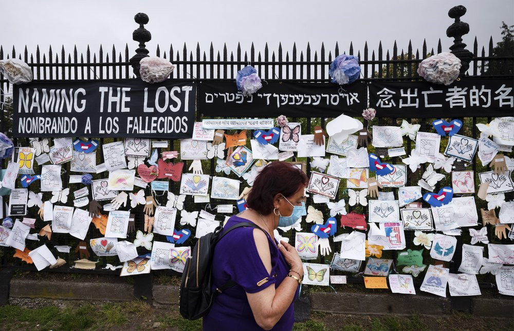 In this May 28, 2020, file photo, a woman passes a fence outside Brooklyn's Green-Wood Cemetery adorned with tributes to victims of COVID-19 in New York.