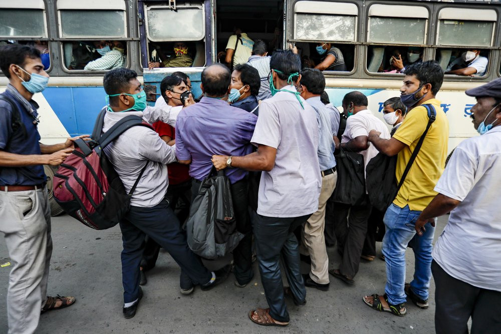 Commuters ignoring physical distancing norms push each other as they try to board on a long distance bus in Kolkata, India, Thursday, Oct. 1, 2020.