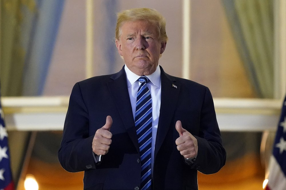 US President Donald Trump stands on the balcony outside of the Blue Room as returns to the White House Monday, Oct. 5, 2020, in Washington, after leaving Walter Reed National Military Medical