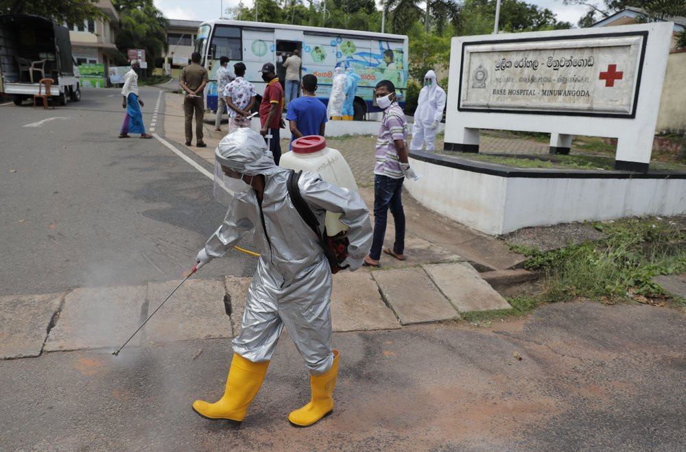 A Sri Lankan health worker sprays disinfectants as people wait to give swab samples to test for COVID-19 near a mobile testing vehicle outside a hospital in Minuwangoda, Sri Lanka, Tuesday, O