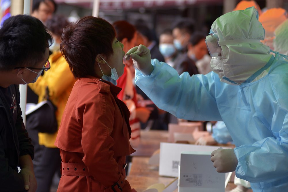 A medical staff takes a swab from a woman as residents line up for the COVID-19 test near the residential area in Qingdao in east China's Shandong province on Monday, Oct. 12, 2020.