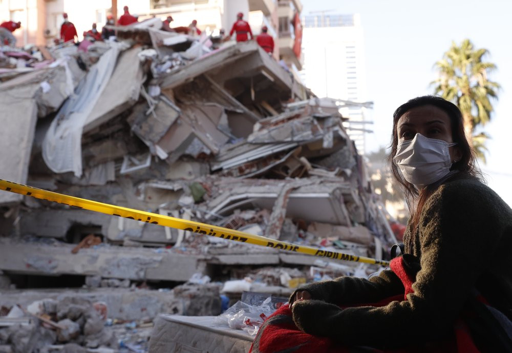A local resident, staying outdoors for fear of aftershocks, watches as members of rescue services search for survivors in the debris of a collapsed building in Izmir, Turkey, Saturday, Oct. 3