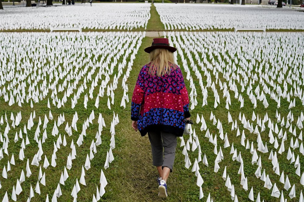 In this Oct. 27, 2020, Artist Suzanne Brennan Firstenberg walks among thousands of white flags planted in remembrance of Americans who have died of COVID-19 near Robert F. Kennedy Memorial St