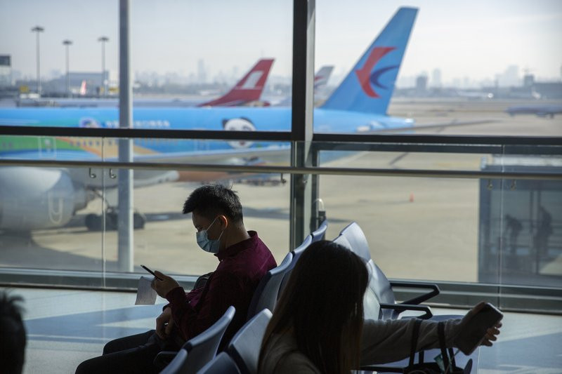 Travelers wearing face masks to protect against the coronavirus sit at a boarding gate at the Shanghai Hongqiao International Airport in Shanghai, Friday, Nov. 6, 2020.