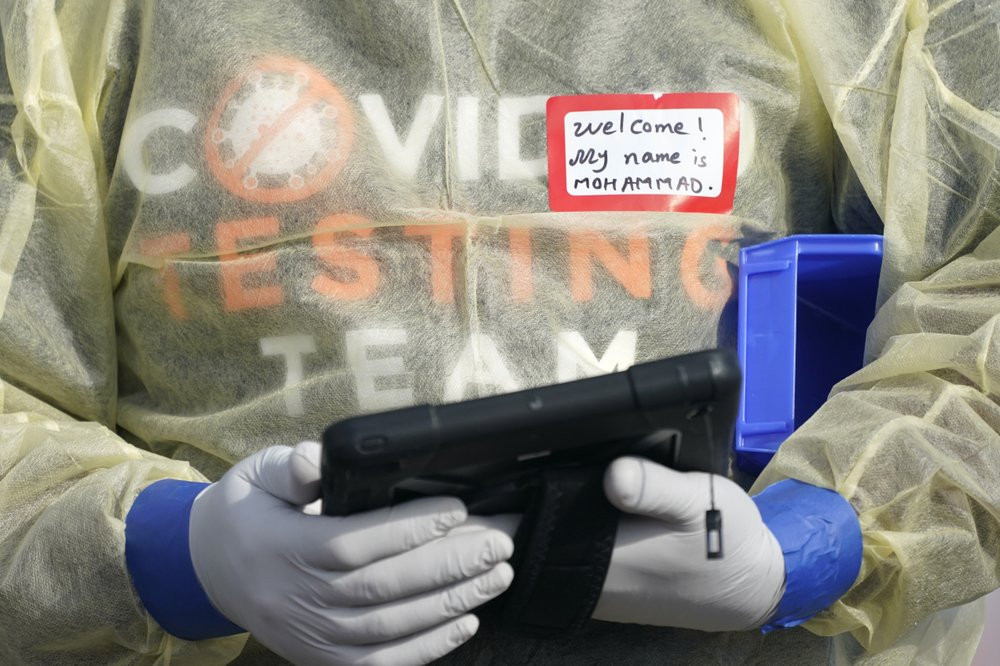 In this Oct. 28, 2020, file photo, a worker wearing gloves, and other PPE holds a tablet computer as he waits to check people at a King County coronavirus testing site in Auburn, Wash., south