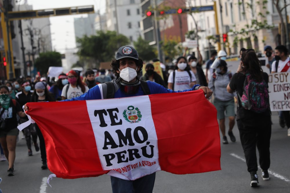 A supporter of ousted President Martin Vizcarra holds a banner with a message that reads in Spanish, "I love you Peru, how could I not," as people refusing to recognize the new government mar