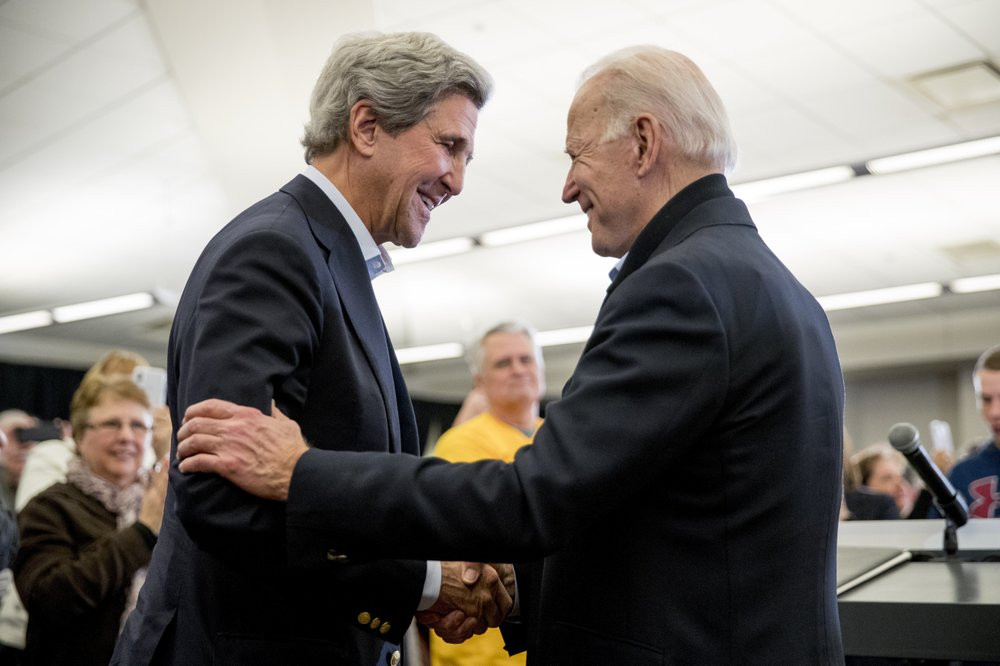 In this Feb. 1, 2020, file photo Democratic presidential candidate former Vice President Joe Biden smiles as former Secretary of State John Kerry, left, takes the podium to speak at a campaig