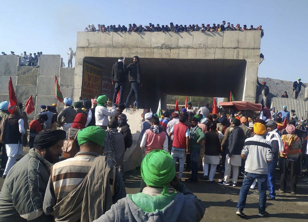 Farmers stand on an under construction flyover and watch attempts of concrete barricades being removed by fellow farmers, set up by security officers to prevent their protest march to Delhi, 