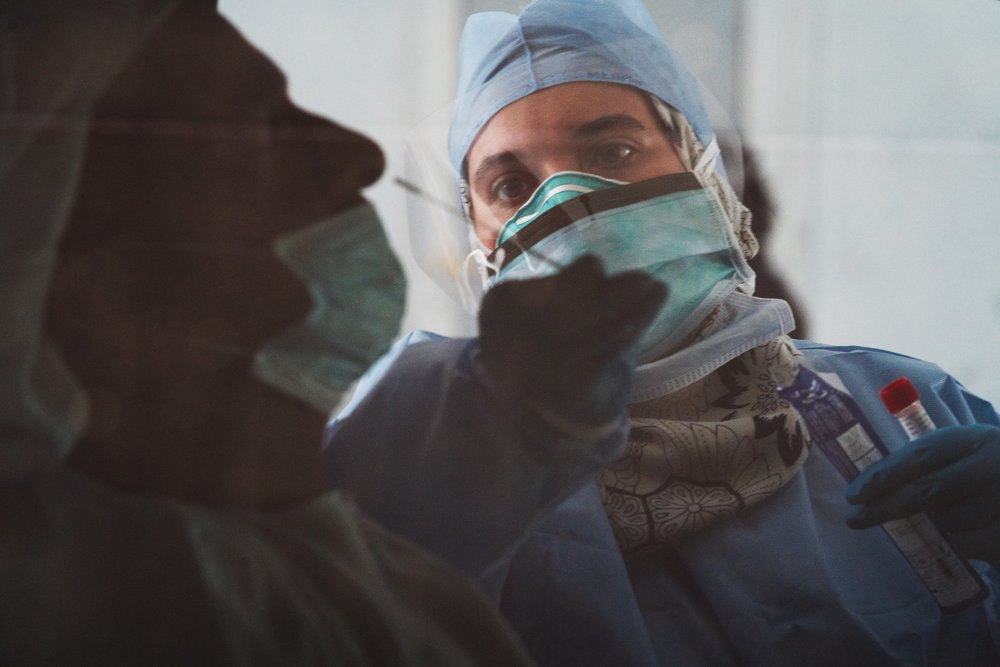 In this April 2, 2020, file photo taken through a tinted car window, a technician takes a nasal swab for a coronavirus detection test at a drive-thru testing facility in Abu Dhabi, United Ara
