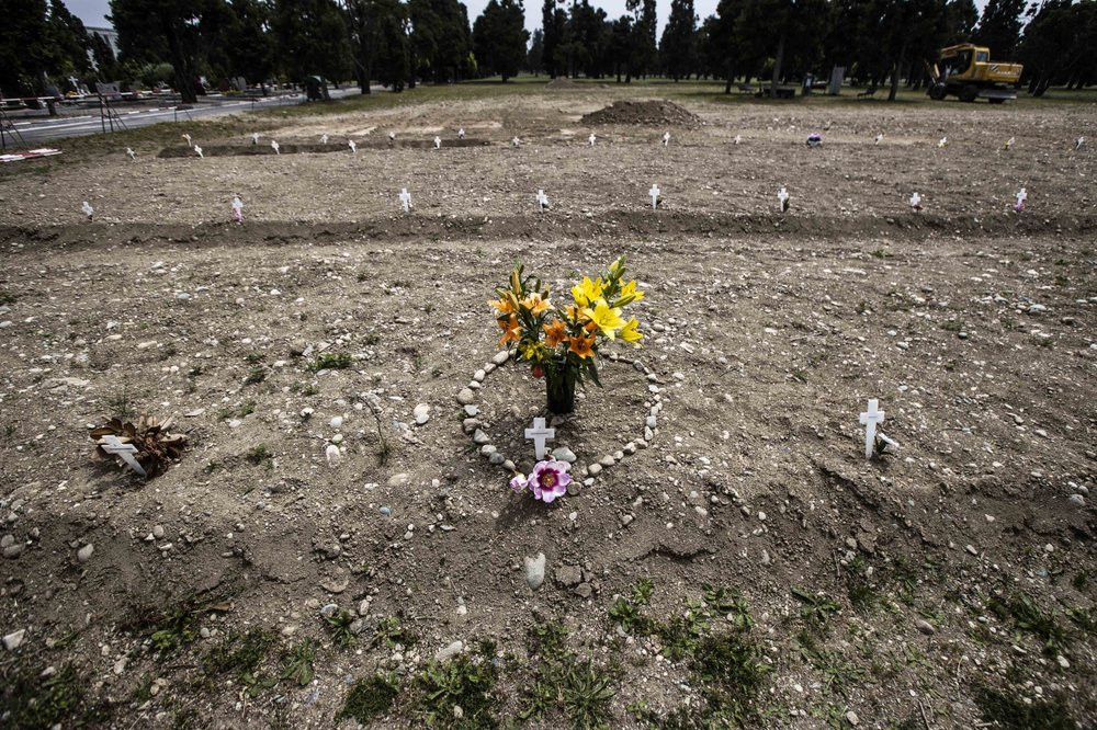 In this May 8, 2020 file photo, flowers and stones placed in the shape of a heart are laid on a burial site as white crosses are scattered at the Campo 81, an area created to host COVID-19 vi