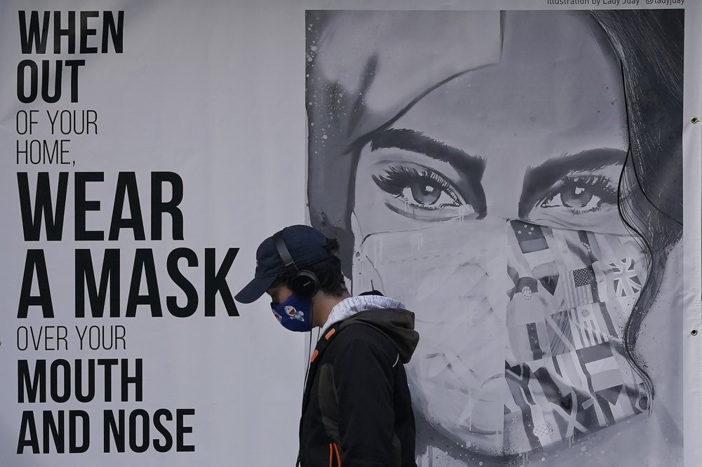 In this Nov. 21, 2020, file photo, a pedestrian walks past a mural reading: "When out of your home, Wear a mask over your mouth and nose," during the coronavirus outbreak in San Francisco.