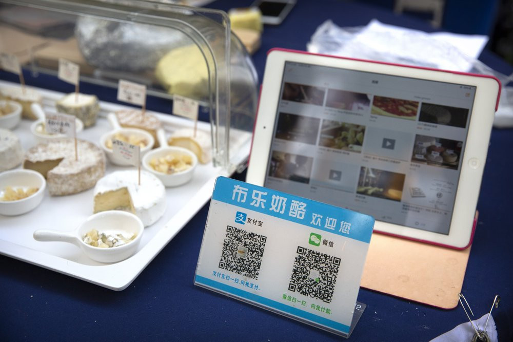 A card displaying QR codes to pay electronically with WeChat Pay and Alipay sits on a vendor's table at a farmer's market in Beijing, Tuesday, Oct. 27, 2020.