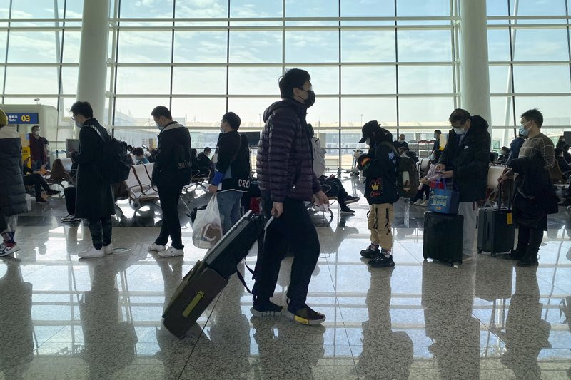 Passengers wearing face masks to protect against the spread of the coronavirus line up at a boarding gate at Wuhan Tianhe International Airport in Wuhan in central China's Hubei Province, Thu