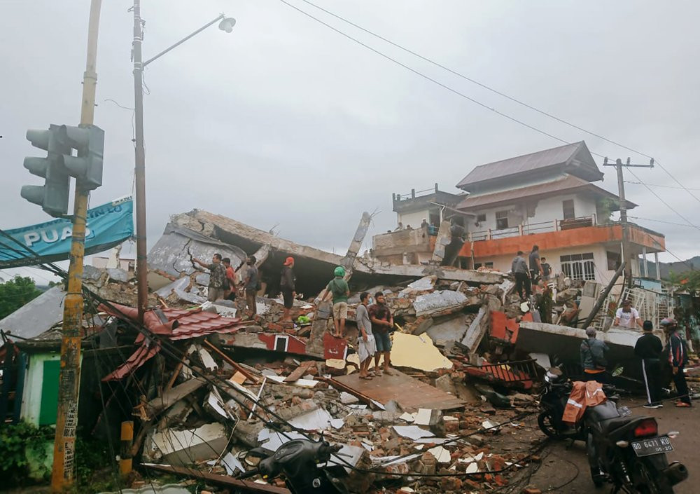 Residents inspect earthquake-damaged buildings in Mamuju, West Sulawesi, Indonesia, Friday, Jan. 15, 2021.