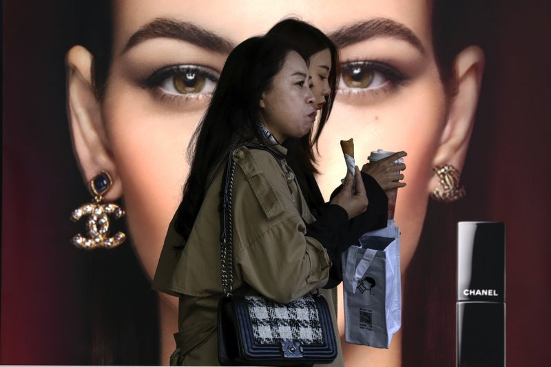 In this Oct. 19, 2020, file photo, women eating snack walk by a Chanel cosmetic shop at the capital city's popular shopping mall in Beijing.
