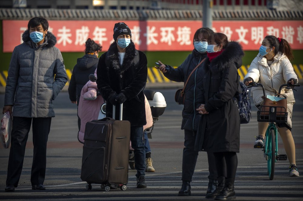People wearing face masks to protect against the spread of the coronavirus wait to cross an intersection in Beijing, Wednesday, Jan. 20, 2021.