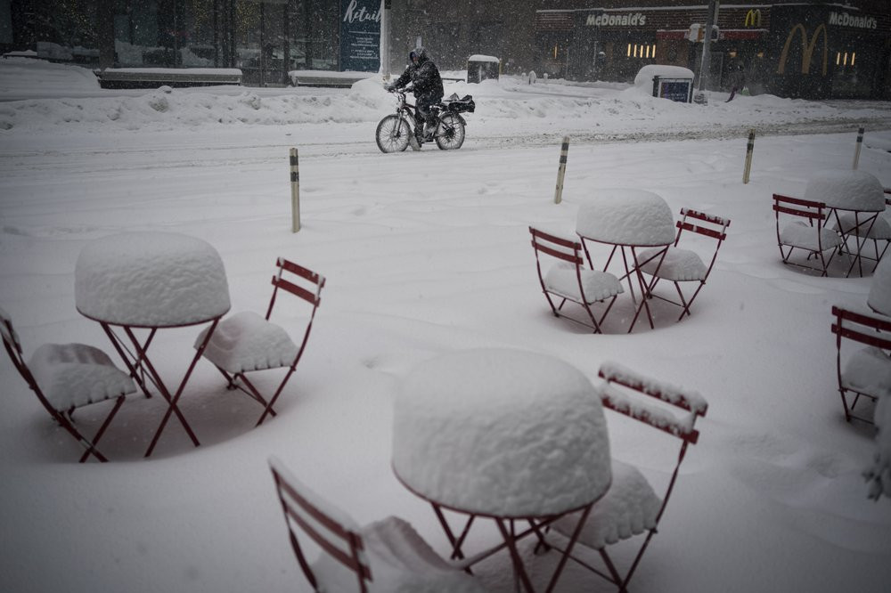 A man delivers food on his electric bicycle as he rides past snow-covered dining tables in midtown during a snowstorm, Monday, Feb. 1, 2021, in New York.