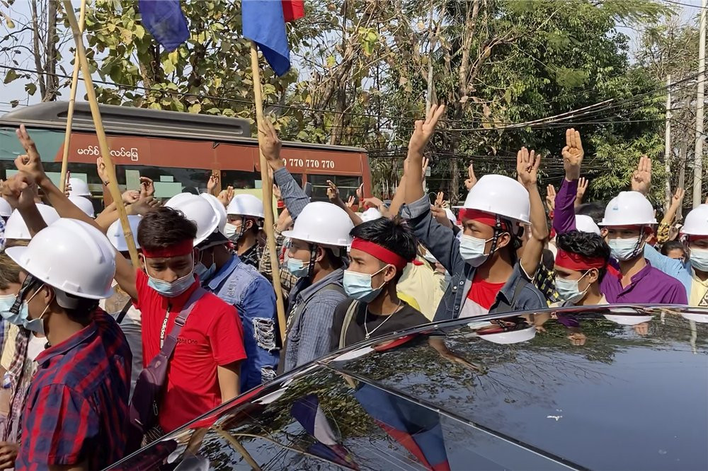 In this image from video, protesters wearing hard hats flash the three-fingered salute while they march in Yangon, Myanmar Saturday, Feb. 6, 2021.