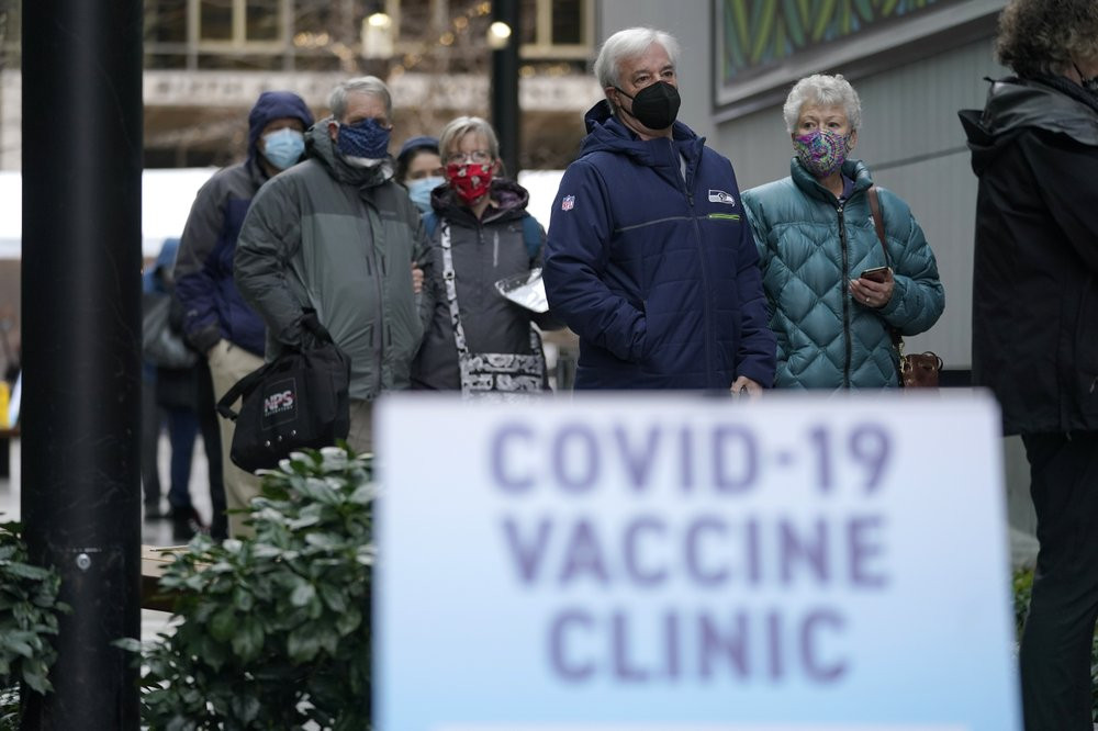 In this an. 24, 2021, file photo, people stand near a sign as they wait in line to receive the first of two doses of the Pfizer vaccine for COVID-19 at a one-day vaccination clinic set up in 