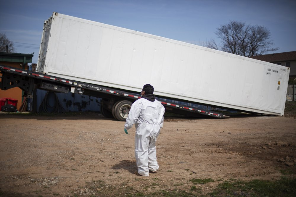 In this April 7, 2020 file photo, gravedigger Thomas Cortez watches as a refrigerated trailer is delivered to keep pace with a surge of bodies arriving for burials at the Hebrew Free Burial A