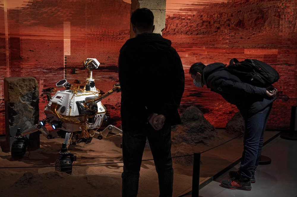 People wearing face masks to help curb the spread of the coronavirus look at a model depicting a rover on Mars during an exhibition at a shopping mall in Beijing on Wednesday, Feb. 24, 2021.