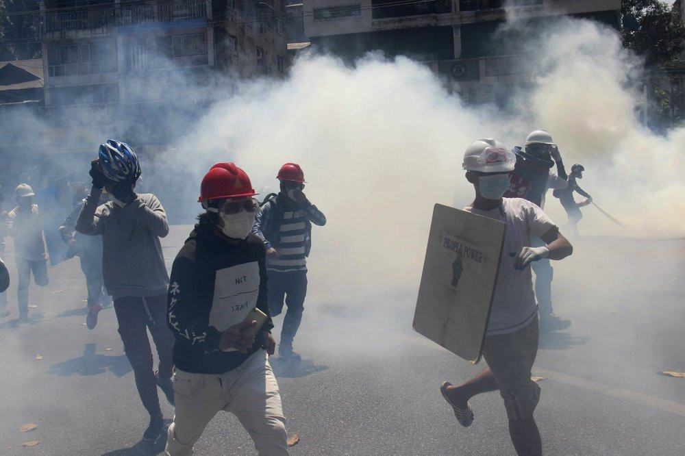 Anti-coup protesters run away from tear gas launched by security forces in Yangon, Myanmar, Monday, March 1, 2021.