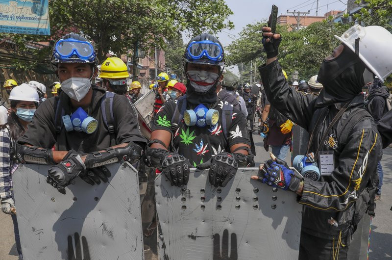 In this March 9, 2021, file photo, anti-coup protesters with makeshift shields take positions while one man looks at his phone in Mandalay, Myanmar.