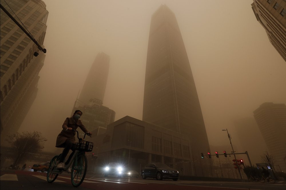 A cyclist and motorists move past office buildings amid a sandstorm during the morning rush hour in the central business district in Beijing, Monday, March 15, 2021.