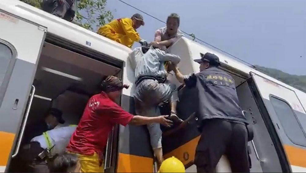 In this image made from a video released by hsnews.com.tw, a passenger, center, is helped to climb out of a derailed train in Hualien County in eastern Taiwan Friday, April 2, 2021.